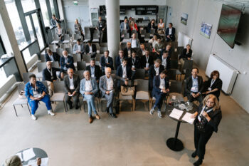 Frau spricht in ein Mikrofon, Publikum im Hintergrund